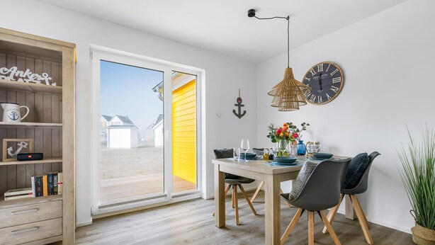 A dining area with a wooden table, two chairs, a clock, and a view through a glass door.