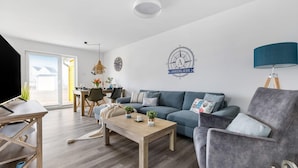 A modern living room with a sofa, armchair, coffee table, and a dining area with a table and chairs.