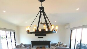 A modern dining area with a large wooden table, white upholstered chairs, and a unique black chandelier with exposed bulbs. - CCV Quivira- 3BR Cozy Home w/ Golf and Restaurants access! (Cabo San Lucas)