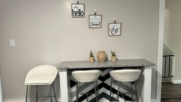 Une cuisine dotée d’un comptoir en granit, de trois tabourets de bar blancs et de trois panneaux décoratifs fixés au mur, portant des phrases inspirantes.