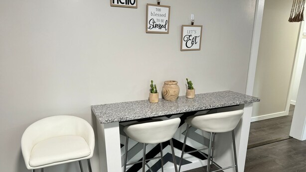 A kitchen with a granite countertop, two white bar stools, and three wall-mounted signs. -  Leave Worries Behind (Wilkes-Barre)