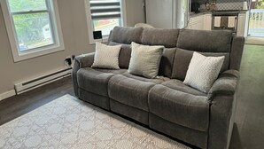 A living room with a grey sofa, a patterned rug, and a kitchen in the background. -  Leave Worries Behind (Wilkes-Barre)