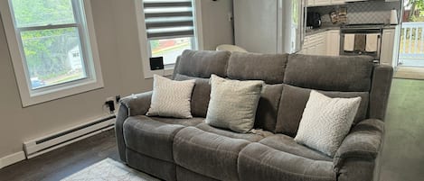A living room with a grey sofa, a patterned rug, and a kitchen in the background.