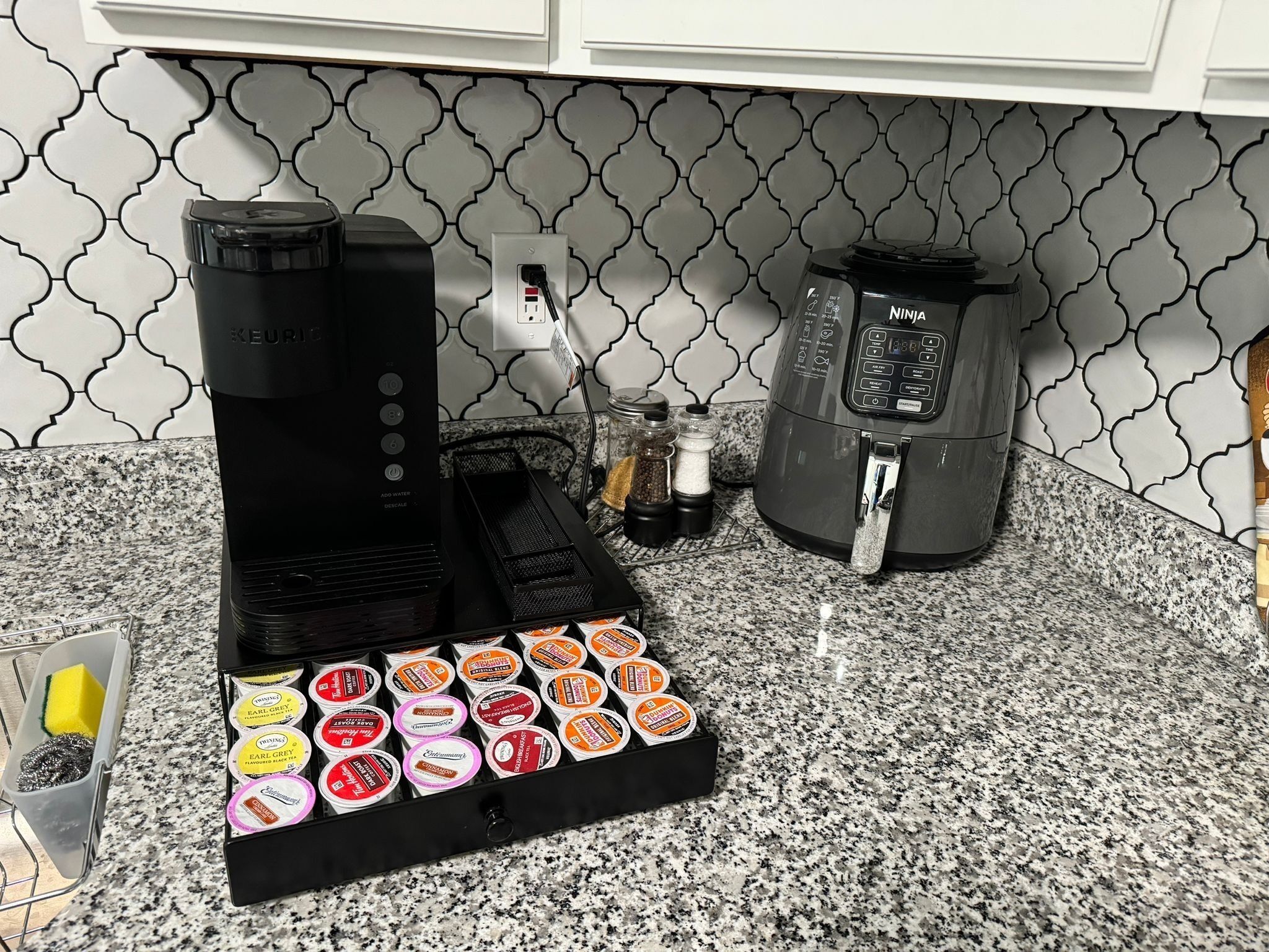 Cozinha com cafeteira, chaleira e suporte para cápsulas de café em bancada de granito.