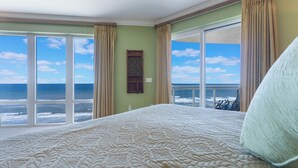 Un dormitorio con una cama grande, vista al océano y una ventana con cortinas.