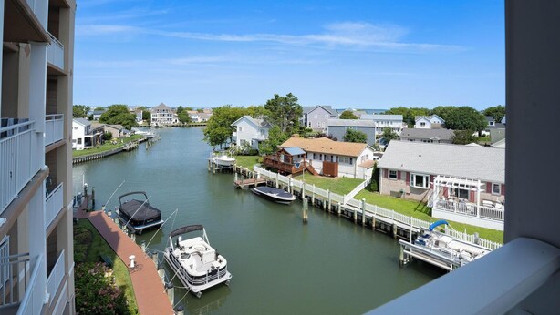 A canal view with boats docked, a house with a dock, and a building with a balcony.