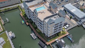 An aerial view of a multi-story hotel with a rooftop pool, adjacent to a marina with docked boats.