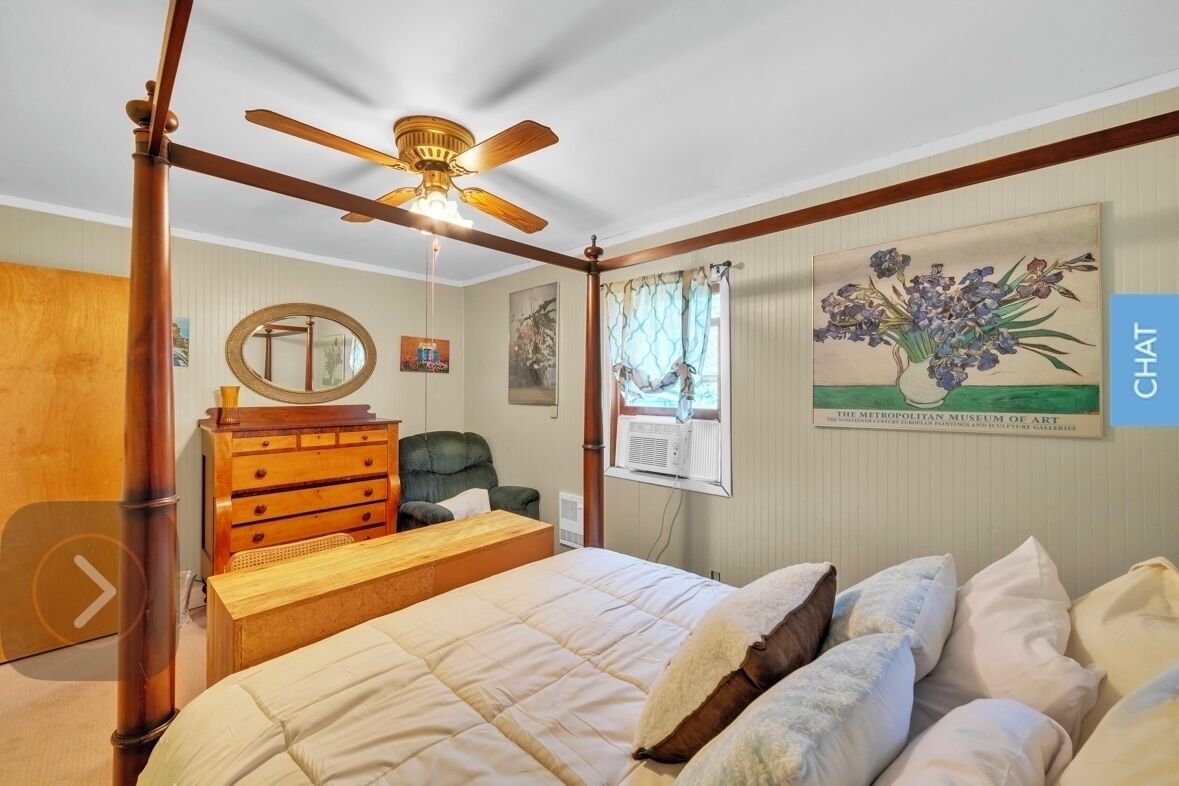 Une chambre à coucher avec un lit à baldaquin, un ventilateur de plafond, une commode en bois, une chaise et un climatiseur fixé au mur.