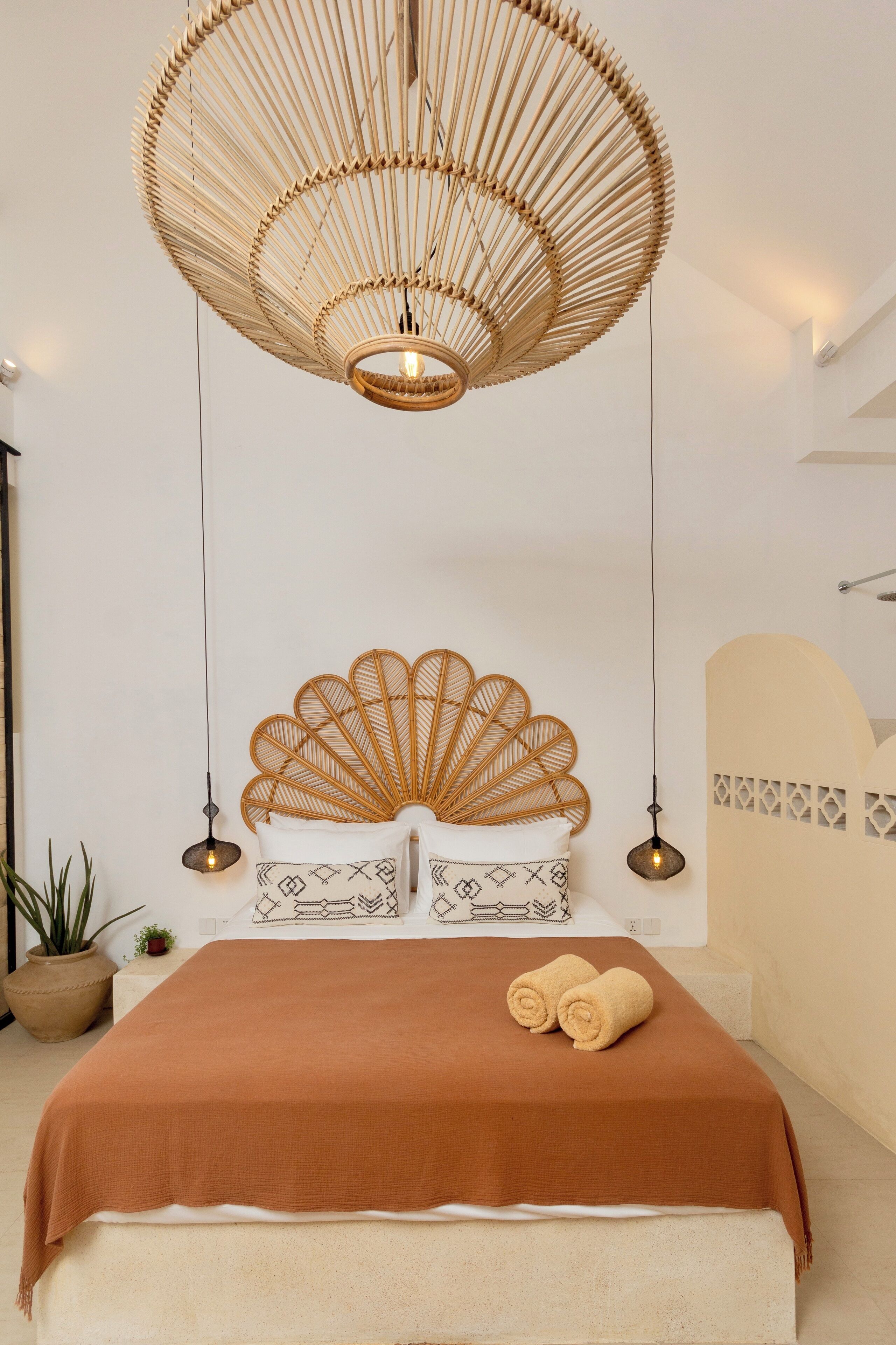 Ein Schlafzimmer mit einem großen Bett, einem Rattan-Kopfstück und einer hängenden Rattan-Lampenleuchte.