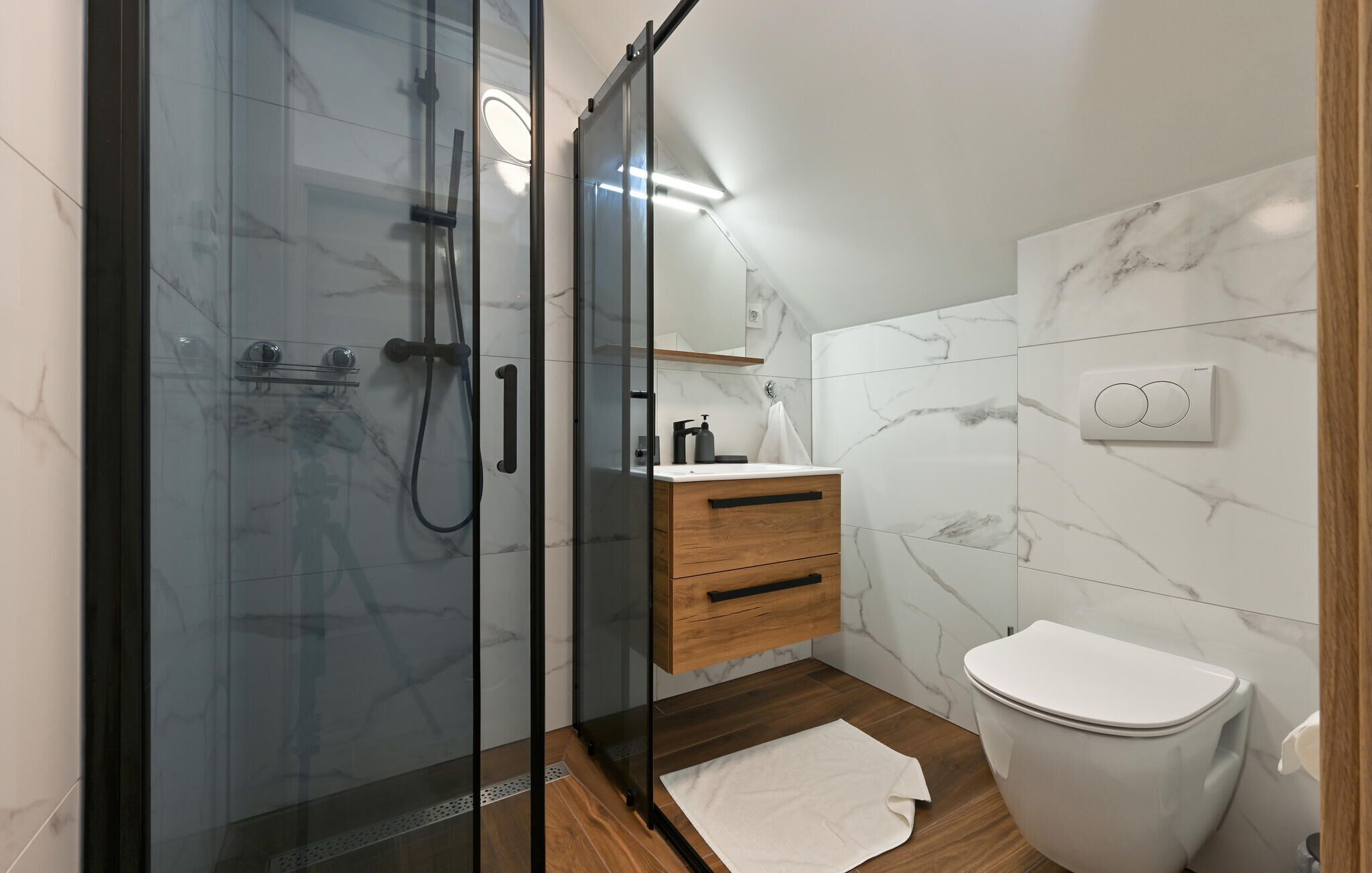 Une salle de bain moderne avec une douche à parois de verre, un meuble-lavabo en bois et des toilettes blanches.