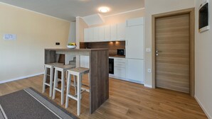Une cuisine moderne avec des armoires blanches, un comptoir en bois et un four à micro-ondes encastré. On y trouve trois tabourets de bar sous un îlot central en bois.