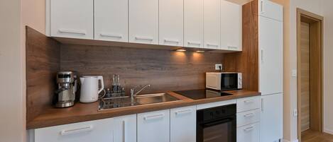 A modern kitchen with white cabinets, a wooden countertop, a built-in oven, a microwave, and a coffee maker.