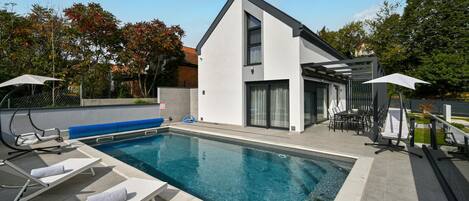 A modern house with a swimming pool, outdoor furniture, and a patio area.