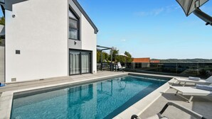 Un espace piscine moderne offrant une vue dégagée sur la piscine, des chaises longues et un bâtiment doté de grandes fenêtres.
