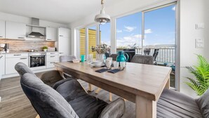 Una cocina moderna con armarios blancos, una estufa y un comedor con mesa de madera y sillas tapizadas en gris.