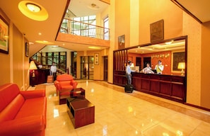 A spacious lobby with a reception desk, a staircase, and a seating area with a red sofa and a coffee table. - Nyaika Hotel Limited (Fort Portal)