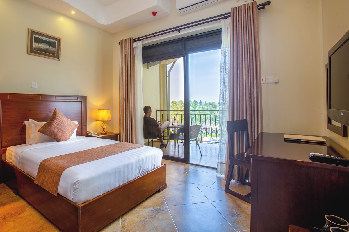 A hotel room with a bed, bedside lamps, a desk with a TV, and a balcony with a view.