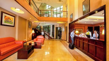 A hotel lobby with a reception desk, a staircase, and a seating area with a sofa and a coffee table.