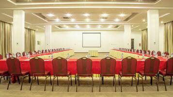 Une salle de conférence avec une longue table, des chaises rouges et un écran de projection.
