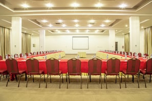 Un salón de conferencias con una larga mesa, sillas rojas y una pantalla de proyector.