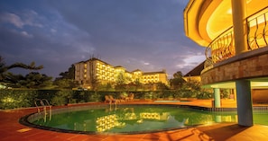 A swimming pool with a reflection of a building, surrounded by greenery and a well-lit balcony. - Nyaika Hotel Limited (Fort Portal)