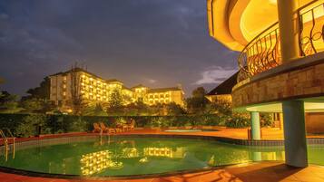 A hotel with a swimming pool, outdoor seating, and a well-lit building at dusk.