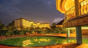 A hotel with a swimming pool, outdoor seating, and a well-lit building at dusk. - Nyaika Hotel Limited (Fort Portal)