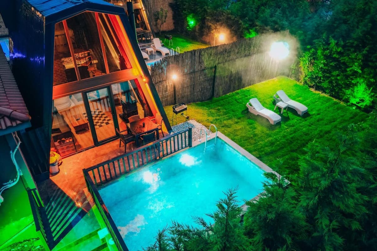 A modern house with a swimming pool, outdoor seating, and a well-maintained lawn.