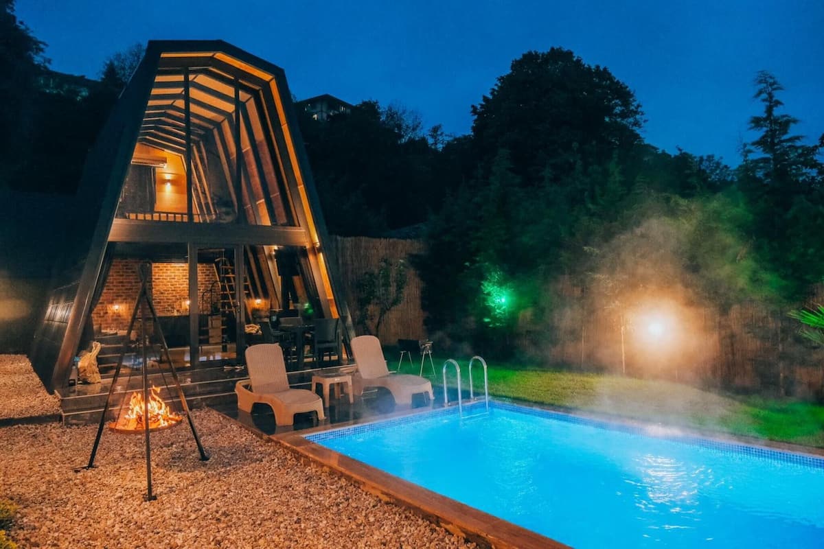 A modern outdoor pool area with a unique geometric structure, a fire pit, and seating.