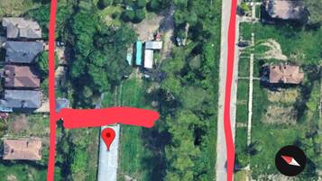 An aerial view of a residential area with a large green space, a marked location, and a road running parallel to the buildings.