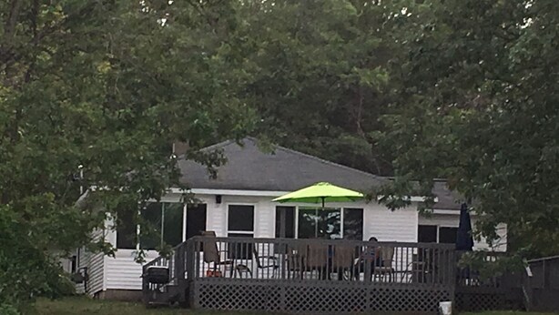 A house with a fenced deck, a green umbrella, and a staircase leading to the deck. - Lakefront two bedroom cottage with Wifi  and Ac on enchanting Idlewild Lake (Idlewild)