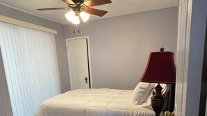 A bedroom with a bed, a ceiling fan, a nightstand with a lamp, and a door. - Lakefront two bedroom cottage with Wifi  and Ac on enchanting Idlewild Lake (Idlewild)