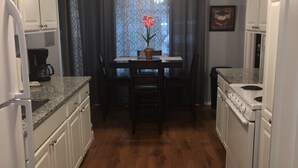 A kitchen with white cabinets, a wooden floor, a dining table with chairs, a ceiling fan, and a coffee maker. - Lakefront two bedroom cottage with Wifi  and Ac on enchanting Idlewild Lake (Idlewild)