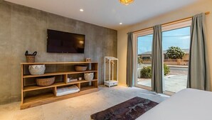 Ein modernes Schlafzimmer mit einem großen Flachbildfernseher, Holzregalen mit Körben, einer Felldecke und Blick ins Freie durch große Fenster.