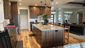 A modern kitchen with wooden cabinets, a granite countertop island, and a dining area with a bench and ottomans. - Comfortable 3-bedroom house with WiFi in Nampa. (Nampa)