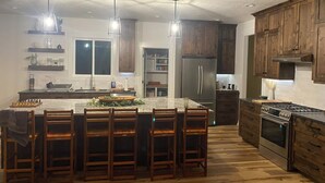 A modern kitchen with a central island, wooden bar stools, stainless steel appliances, and pendant lighting. - Comfortable 3-bedroom house with WiFi in Nampa. (Nampa)