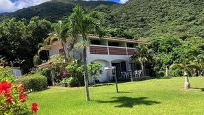 A two-story building with a red-tiled roof, surrounded by lush greenery and a mountain backdrop. - South Sea Ishigaki (Ishigaki)