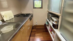 A compact kitchen with a gas stove, stainless steel sink, and wooden cabinets. There is a window with blinds, a built-in oven, and a refrigerator. - South Sea Ishigaki (Ishigaki)
