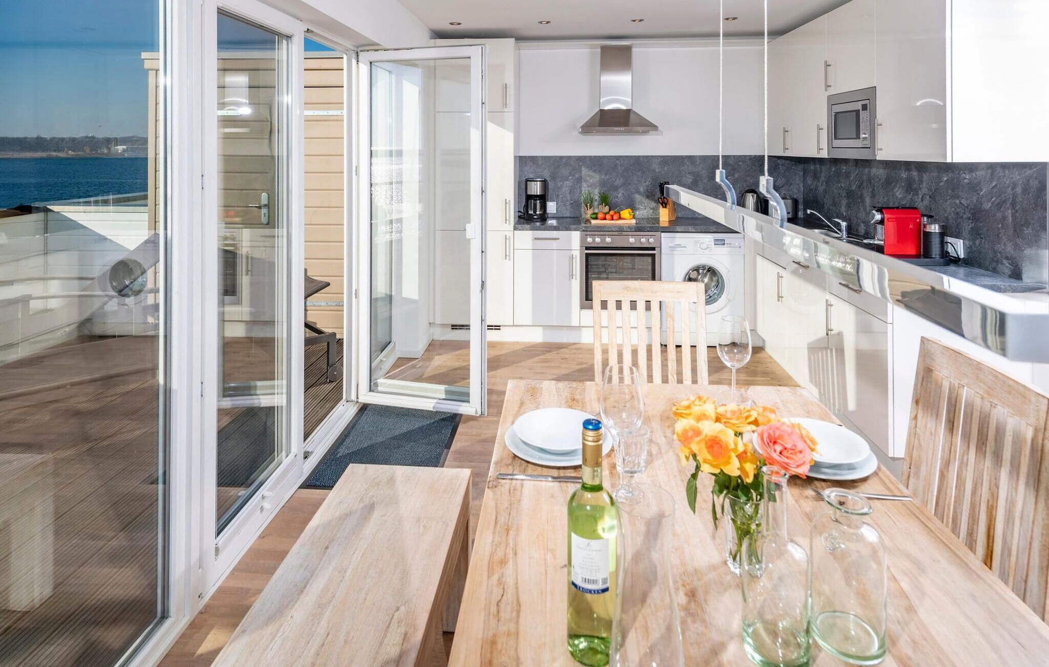 Et moderne køkken med havudsigt, et spiseområde med et bord dækket til to, og en skydedør til en balkon.