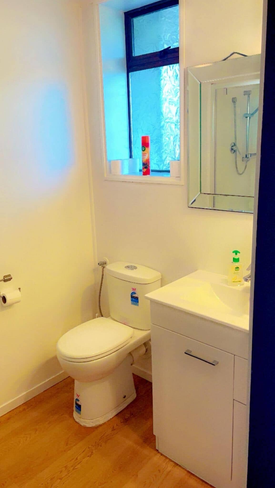 Un baño pequeño y limpio con inodoro, lavamanos y una ventana sobre el inodoro.