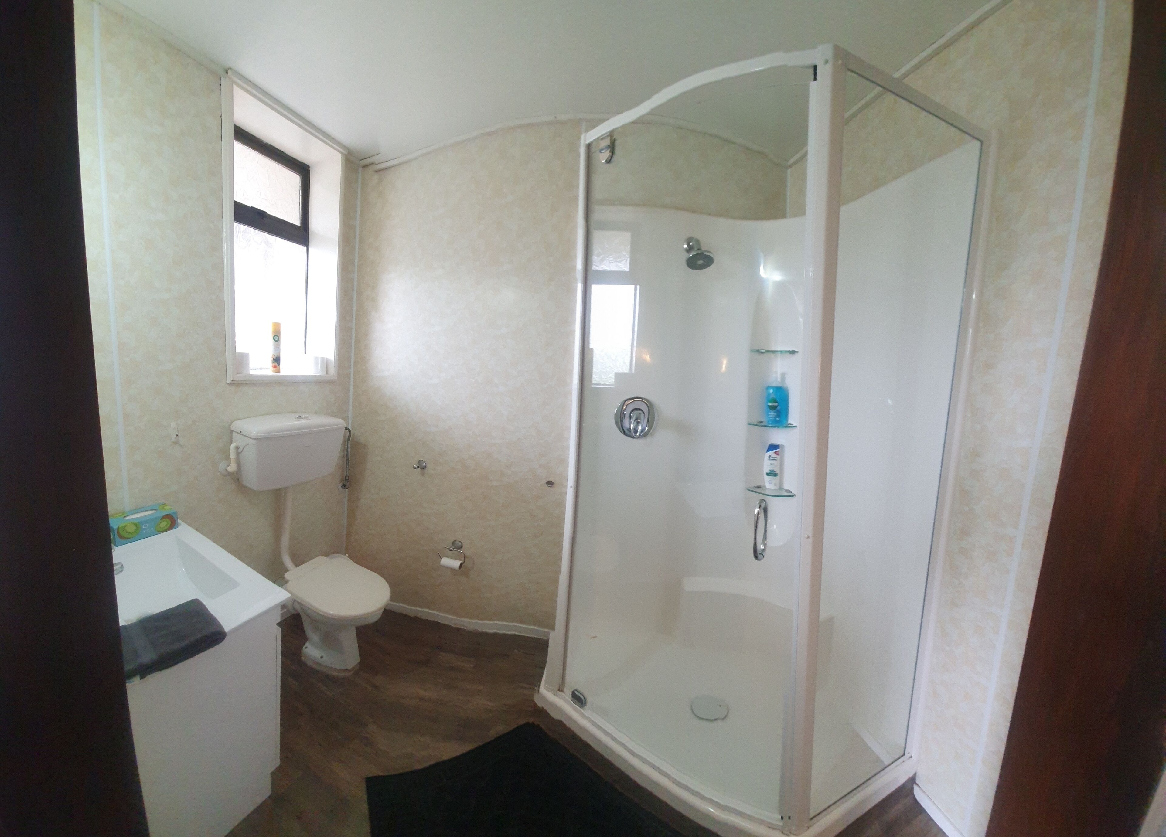 A bathroom with a glass-enclosed shower, a toilet, and a sink with a window above the toilet.