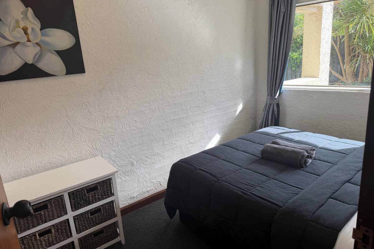 A bedroom with a bed, a white dresser, a wall-mounted painting, and a window with curtains.