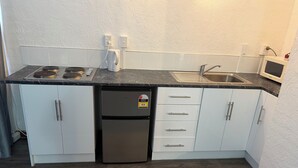 Een compacte keuken met witte kastjes, een roestvrijstalen koelkast, een magnetron en een spoelbak.
