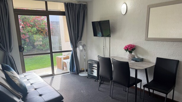 Een kamer met een bank, een tafel met stoelen, een televisie en een raam met gordijnen.