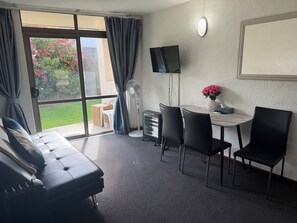 A room with a sofa, a table with chairs, a TV, and a window with curtains. - Mana Motel (Porirua)