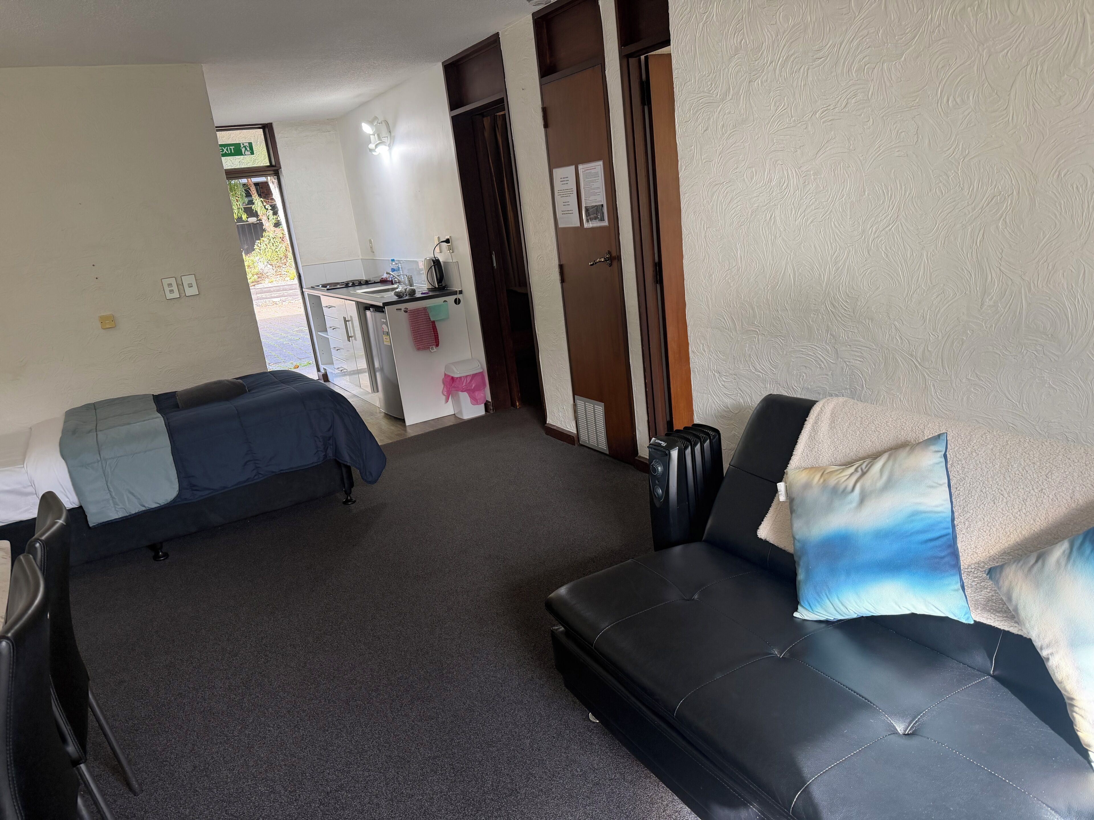 A room with two beds, a sofa, a kitchenette, and a door leading to another room.