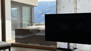 Un salón moderno con un televisor de pantalla plana grande, muebles de mimbre y vistas a un paisaje montañoso a través de amplios ventanales.