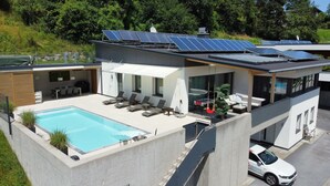 Una casa moderna con piscina en la azotea, paneles solares y un coche aparcado fuera.
