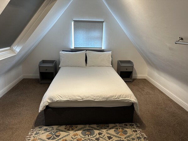 A bedroom with a bed, two bedside tables, a window, and a carpeted floor.