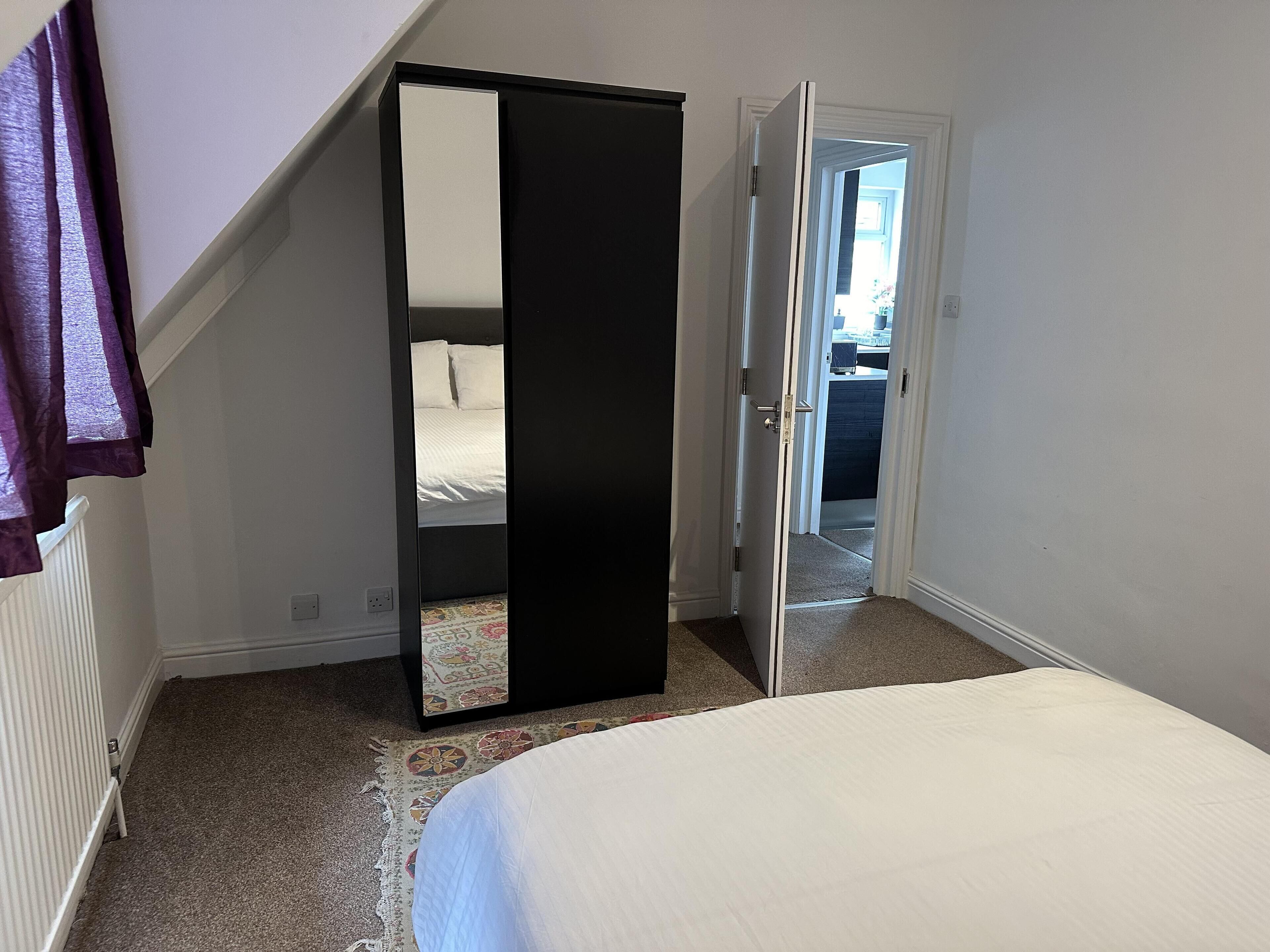A bedroom with a bed, a large mirror, and a door leading to another room.